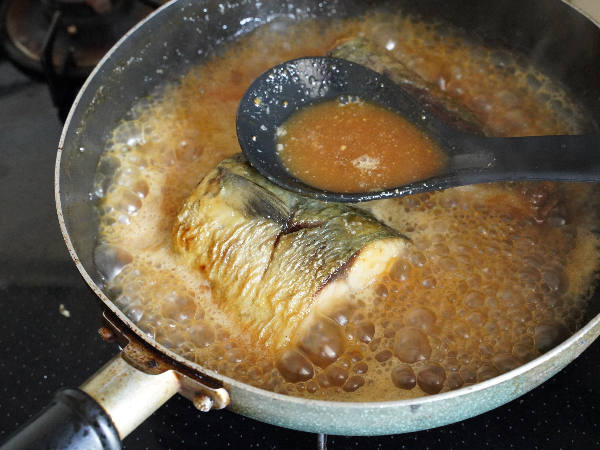 煮汁を鯖にかけながら煮ている様子